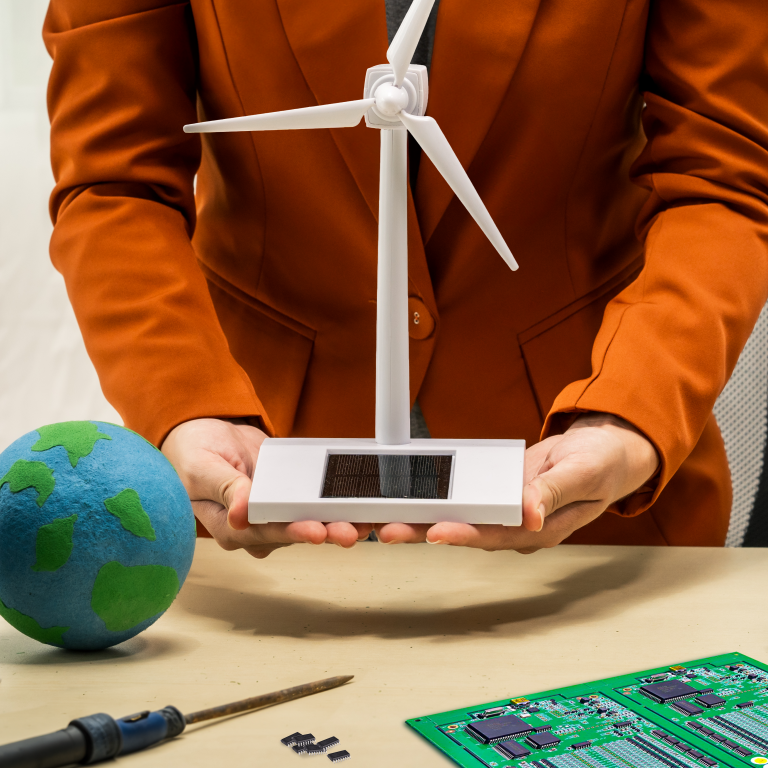 Business woman holding a model wind turbine with a repaired circuit board/PCB on the desk next to soldering iron and some integrated circuit chips. A metaphor for how electronics repair benefits renewable energy sustainability.