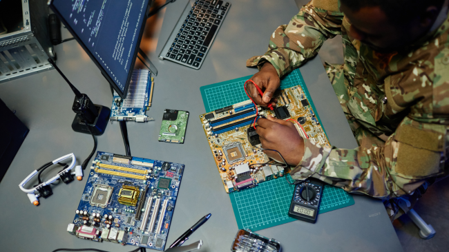 Above angle of young man in military uniform repairing motherboard