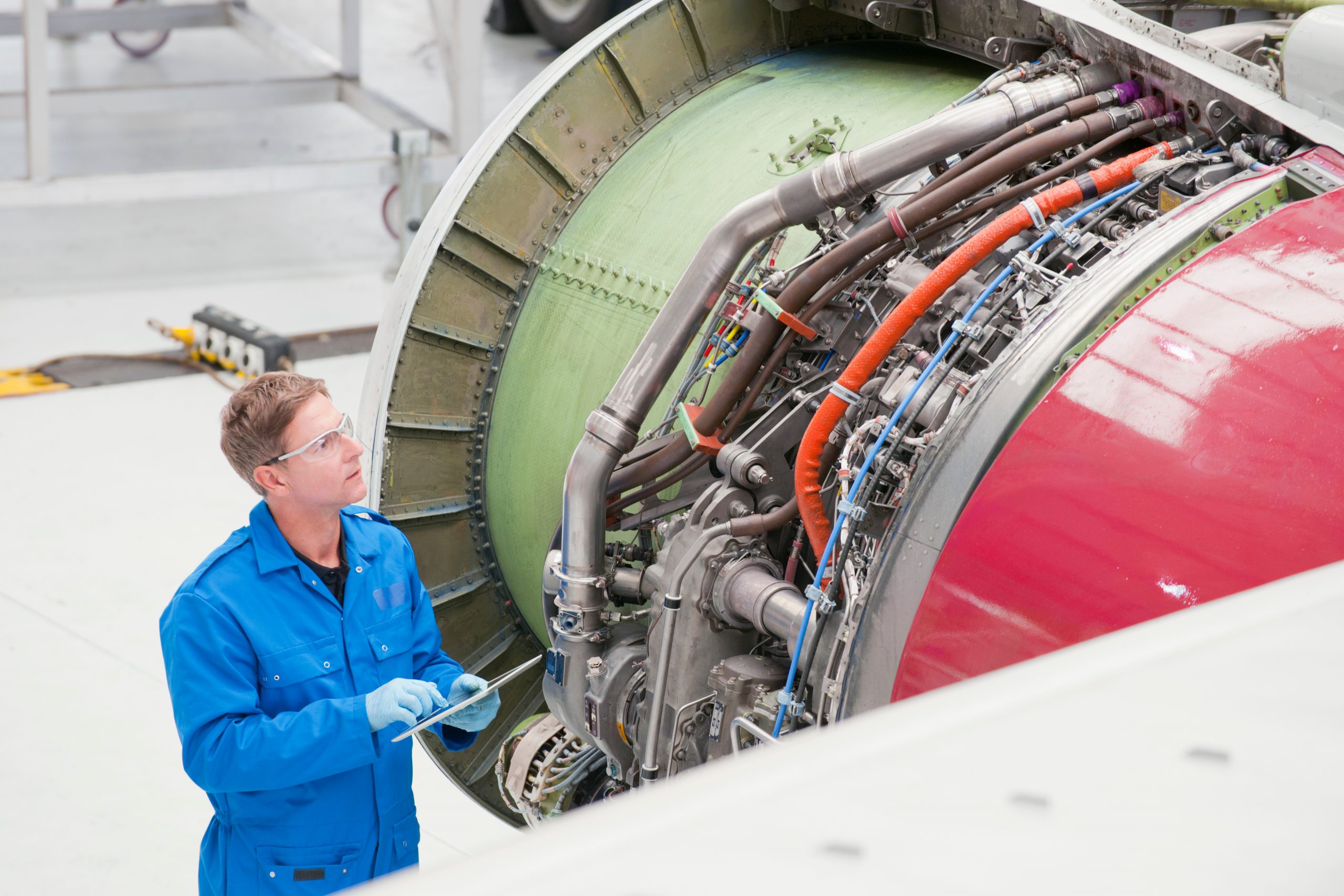 Aircraft mechanic inspecting a jet engine inside an aircraft hangar, examining components during maintenance on a commercial airplane.